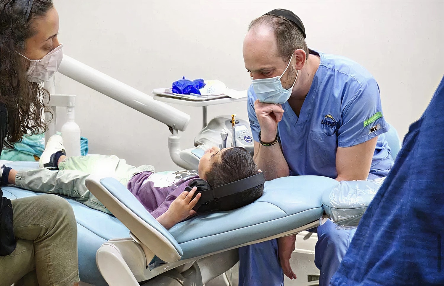 Child receiving dental care with comforting adults.