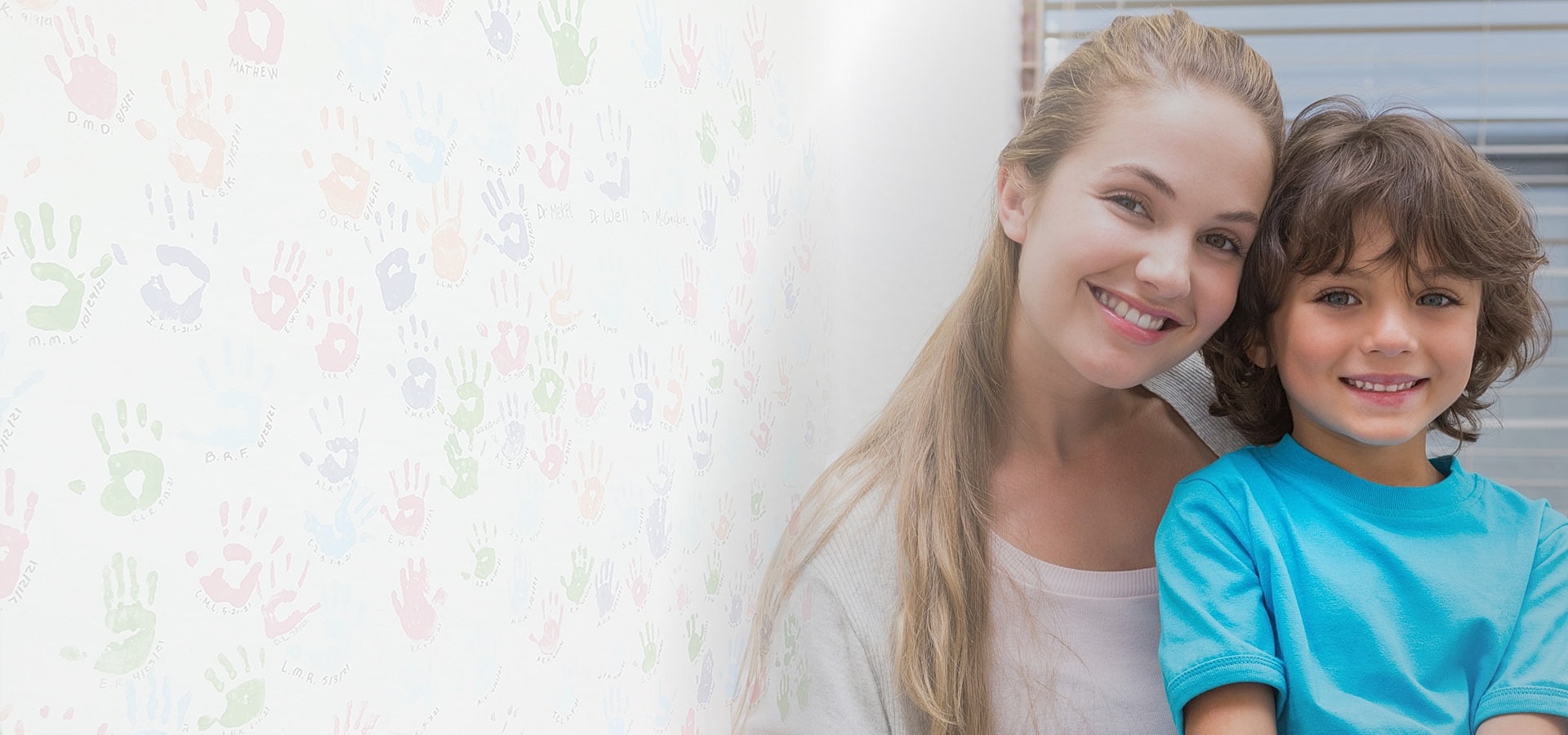 Smiling mother and son with colorful handprint wall.